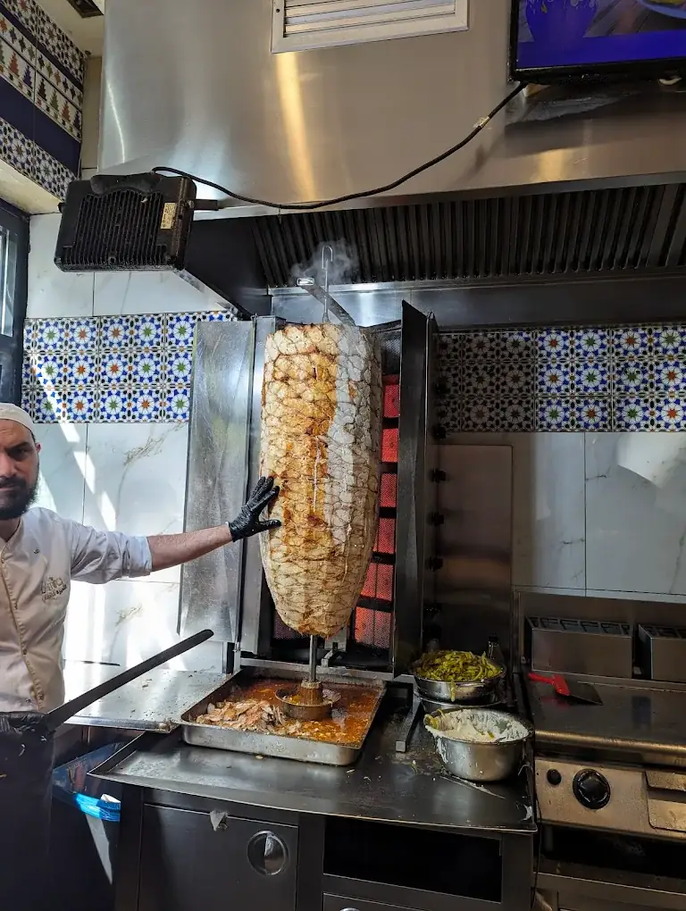 Grillmeister schneidet frisches Hähnchen-Schawarma vom Drehspieß in der Küche von L’Amira City